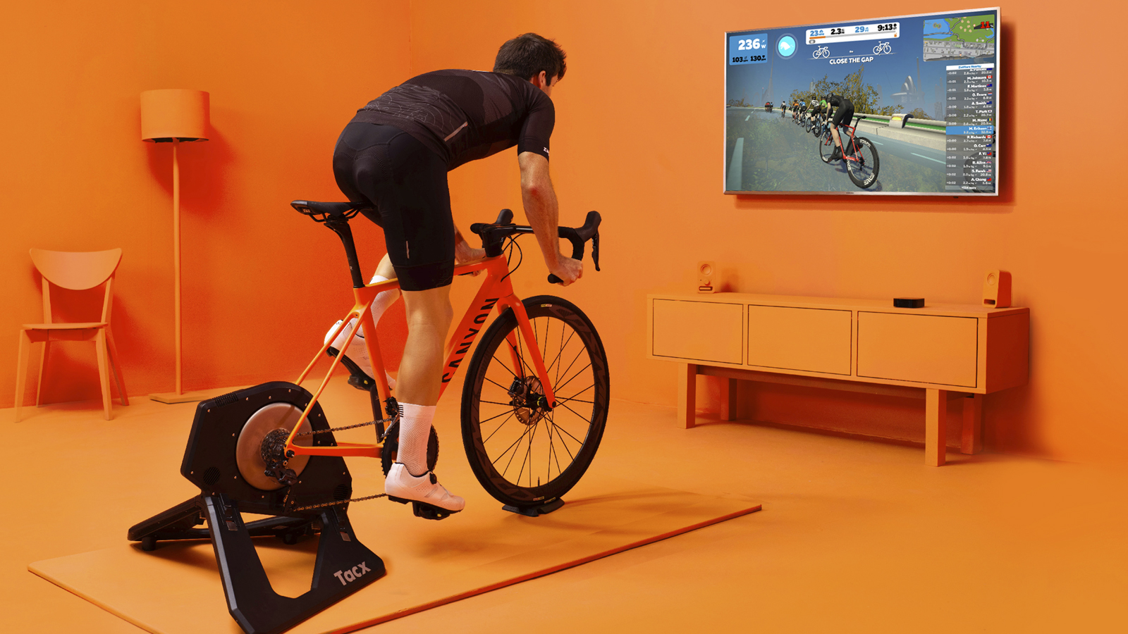 A picture of a man riding an indoor trainer with a screen in front of him showing a virtual cycling world